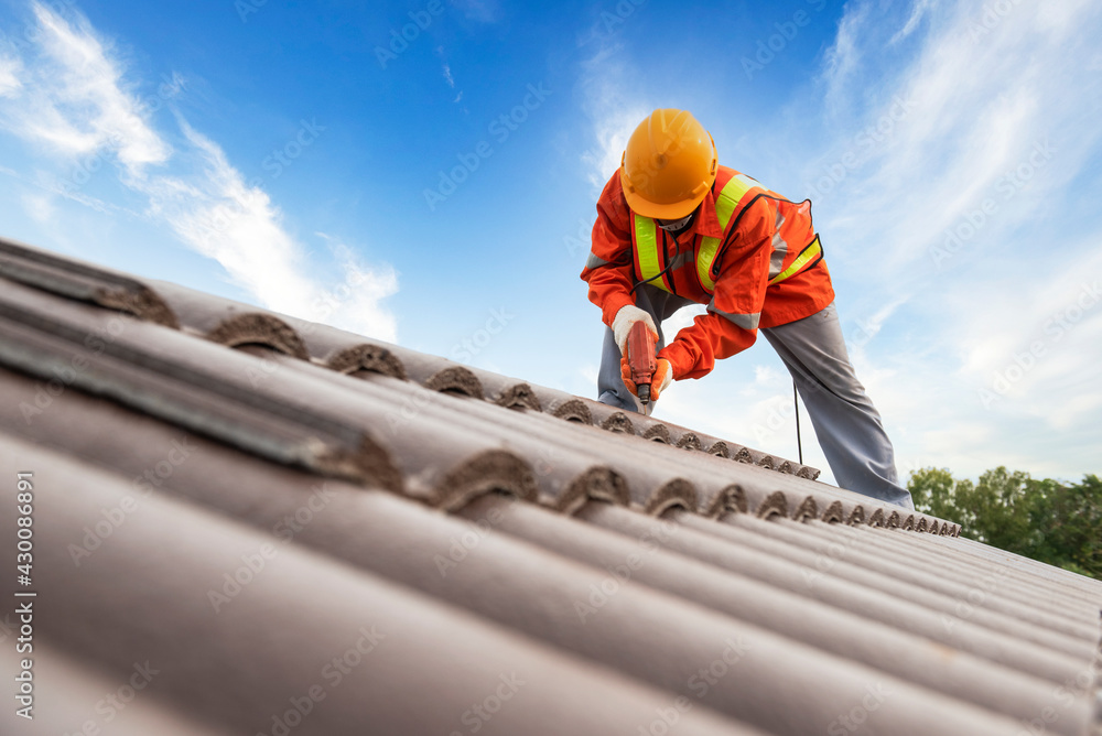 Roofer in high vis clothing and helmetrepairing a tile roof
