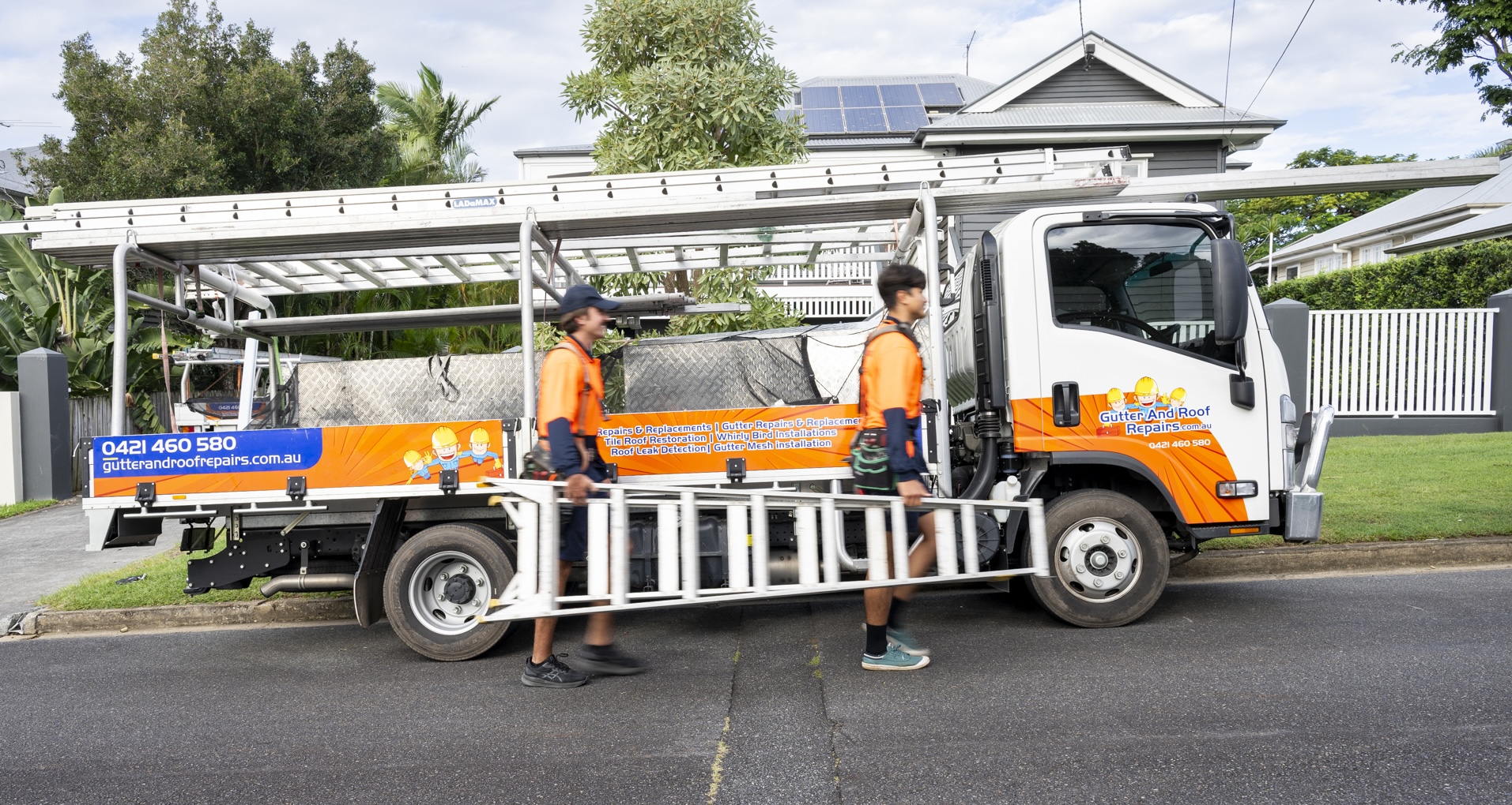 Two Gutter and Roof Repairs roofers carrying ladder in front of work truck
